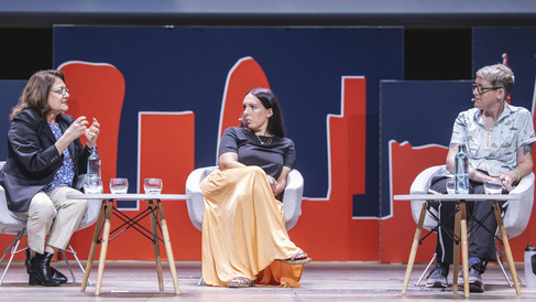 Three speakers sitting and debating on stage, during an event.